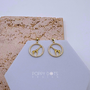 A pair of sterling silver gold-plated giraffe stud earrings encircled by zirconia stones, displayed on a beige background.