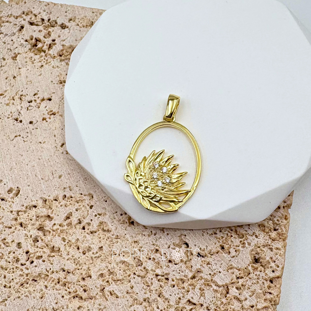 A sterling silver gold plated pendant in the shape of a Protea flower adorned with zirconias, displayed on a white stand.