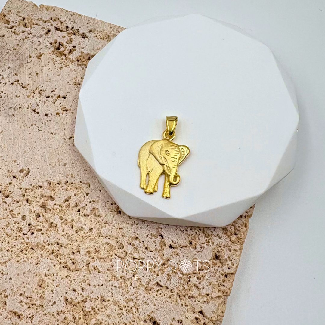A sterling silver gold-plated elephant pendant displayed on a white stand against a textured background.