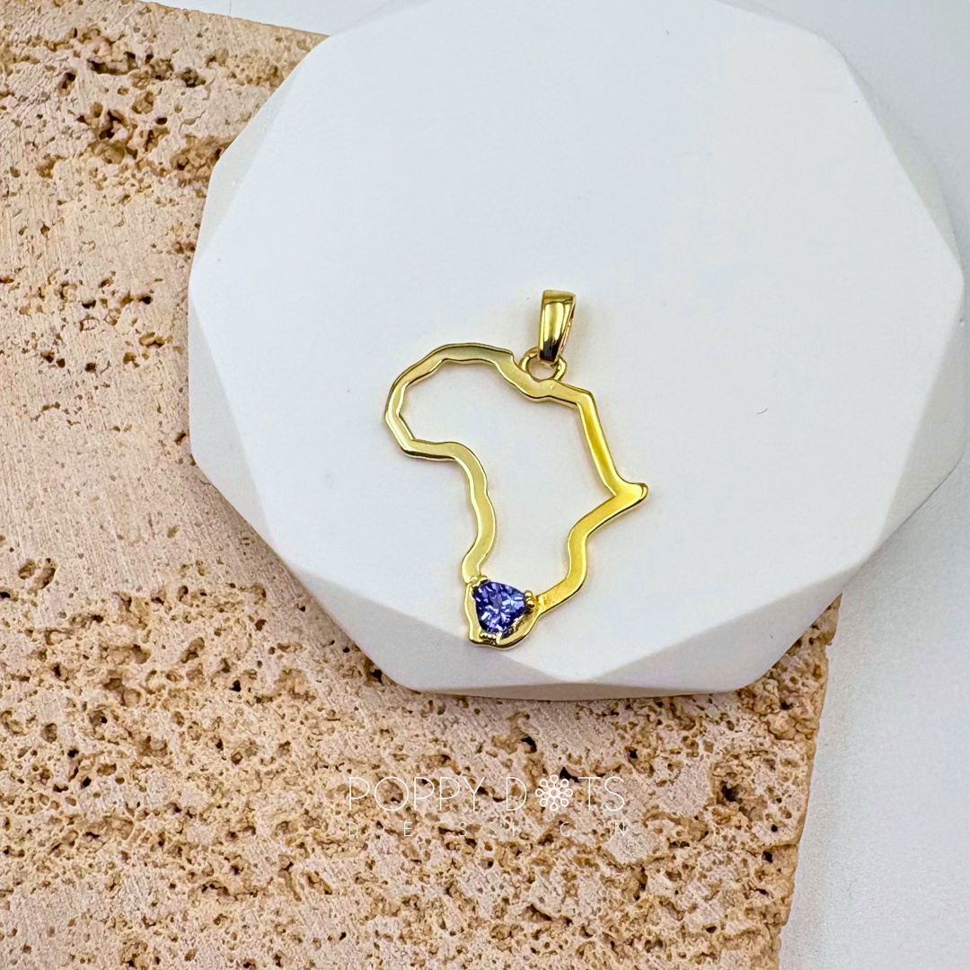 A sterling silver gold-plated pendant in the shape of Africa with a trillion cut Tanzanite gemstone set in the center, displayed on a white platform.