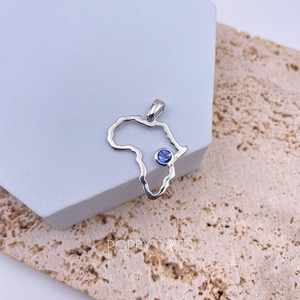 A sterling silver pendant in the shape of Africa with a round tanzanite gemstone in the center, displayed on a white surface.