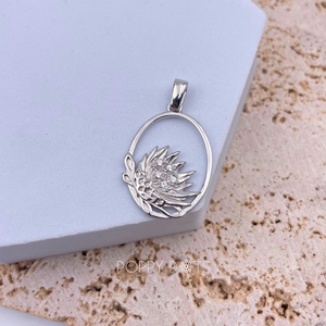 A sterling silver pendant featuring a Protea flower design with zirconias, placed on a textured surface.