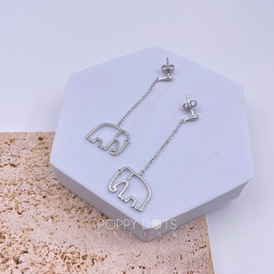 A pair of sterling silver dangling elephant stud earrings displayed on a white stand against a textured background.
