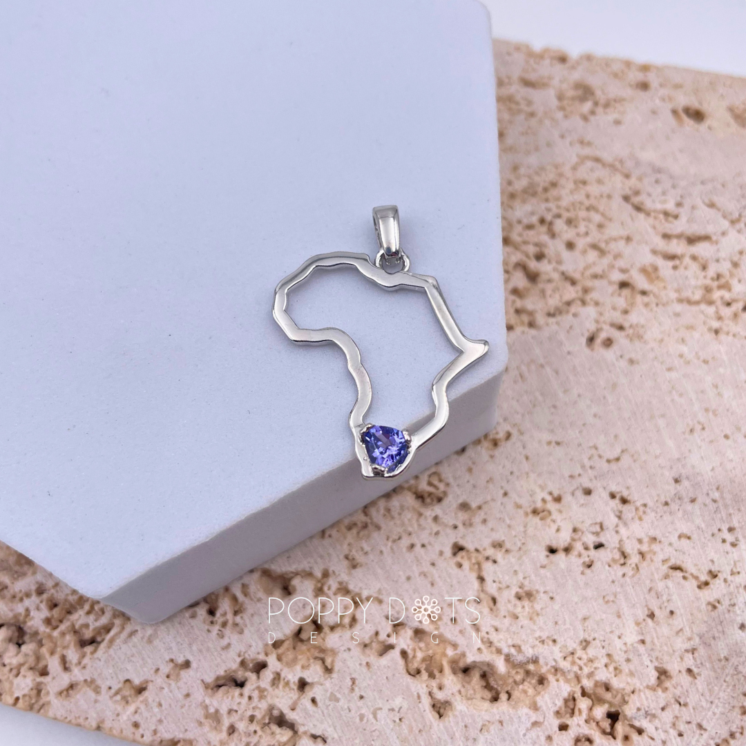 Sterling silver pendant in the shape of Africa with a trillion cut Tanzanite gemstone set in the center, displayed against a neutral background.